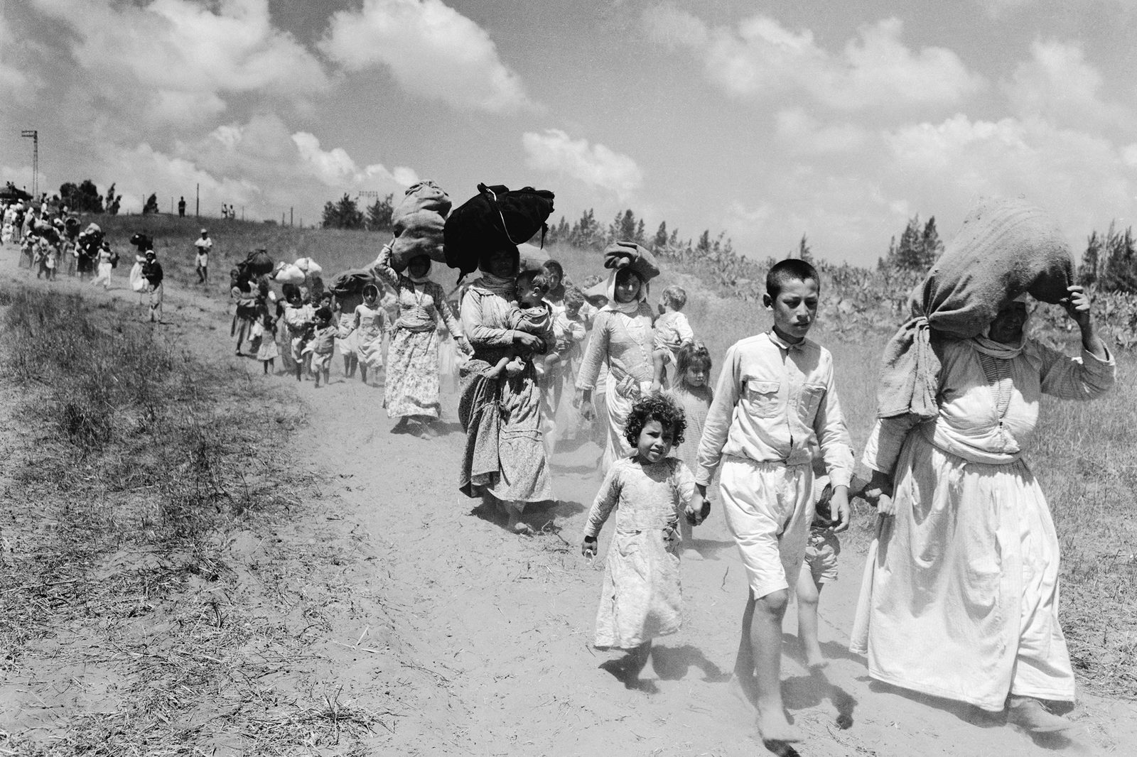 A long line of Palestinian Arab refugees, many carrying belongings, walking along a dirt road during the 1948 war.